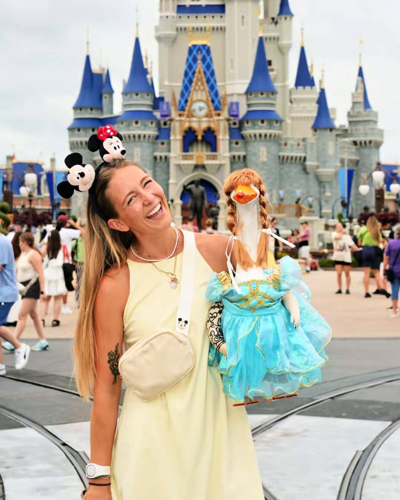 Liz laughing in front of Cinderella Castle, holding Lucy Goosey in a teal ball gown